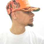 Model wearing an orange camo trucker hat